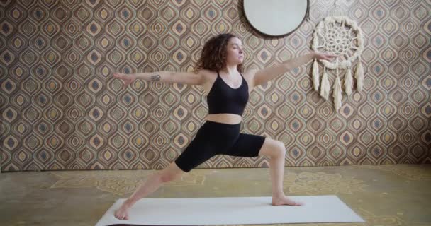 Deportiva mujer de pelo rizado hace ejercicios de estiramiento de yoga. Chica delgada hace yoga en una sala de yoga luminosa y atmosférica por la mañana — Vídeos de Stock