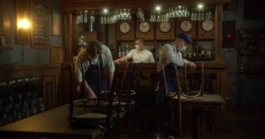Barmen ve Personel yüz maskesi takıp karantinadan sonra restoranı yeniden açmaya hazırlanıyorlar. Önlüklü, koruyucu maskeli ve eldivenli genç garsonlar açık olmadan önce kafede mobilya düzenliyorlar. Konsept: