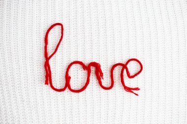 Beyaz örgü arka planında kırmızı yün iplikle yazılmış kelime aşkı. Sevgililer Günü