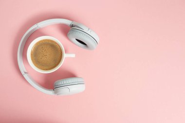 Müzik ya da podcast arka planda kulaklık ve pembe arka planda bir fincan kahve, düz yatak. Üst manzara, düz uzanma