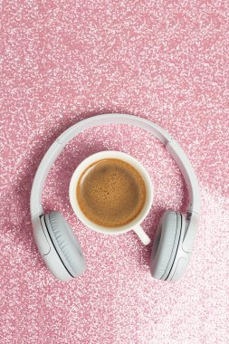 Müzik ya da podcast arka planı, kulaklıklar ve pembe parlak arka planda bir fincan kahve. Üst manzara, düz uzanma