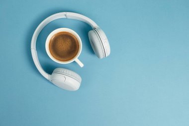 Müzik ya da podcast arka planda kulaklık ve mavi arka planda bir fincan kahve. Üst manzara, düz uzanma