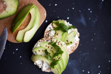 Fresh crisp bread with cream cheese, avocado and seeds on a black background. Vegetarian and diet food. Weight loss diet
