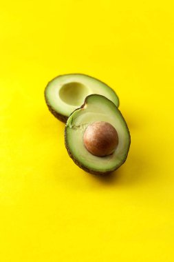 Avokado yarıları sarı arka planda. Tohumlu organik avokado. Boşluğu kopyala