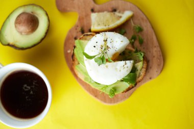 Bir fincan sade kahve ve avokado, haşlanmış yumurta, tohum ve mikroyeşil sandviç. Sarı arka plan. Uzayı kopyala Sağlıklı kahvaltı.