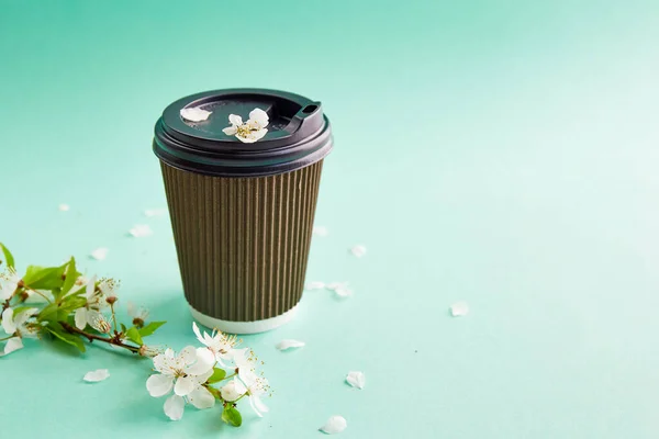 Paper coffee cup with cherry blossom on turquoise background. Closeup blank craft paper coffee cup. Place for text.