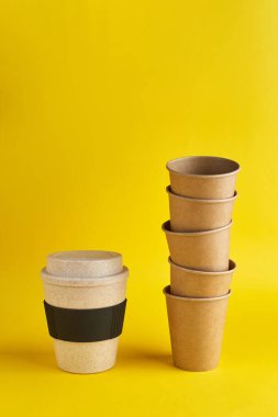 Sıfır israfının modern yolu. Tek kullanımlık bambu kabı bir sürü tek kullanımlık kağıt bardağa karşı. Kahve ve ekoloji. Sarı arkaplan