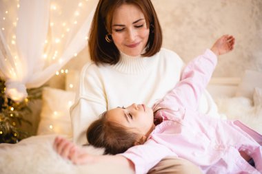 Anne ve kızı, tatil sezonunda yumuşak ışıklı bir odada rahat bir anın tadını çıkarıyorlar.