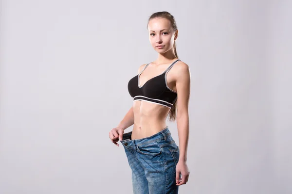 Meisje toont haar gewichtsverlies door het dragen van een oude spijkerbroek — Stockfoto