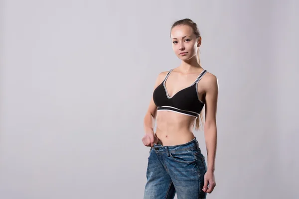 Meisje toont haar gewichtsverlies door het dragen van een oude spijkerbroek — Stockfoto