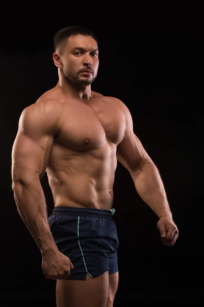 Beau musclé bodybuilder posant sur un fond noir — Photo