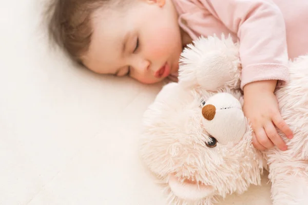 Retrato de cerca de dormir hermosa niña bebé con un oso de peluche esponjoso en la cama — Foto de Stock