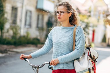 Güneşli bir günde bisikletle üniversiteye giden güzel bir kız öğrenci. Günlük kıyafetli güzel kadın bisiklet sürdükten sonra dışarıda dinleniyor..