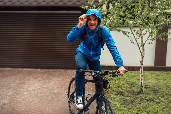 Happy Curly Male Courier Blue Raincoat Delivers Parcel Cycling Bicycle — Stock Photo, Image