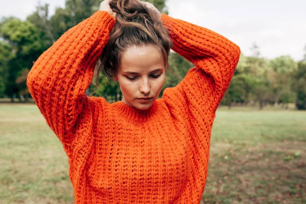 Wanita Muda Dalam Sweater Rajutan Oranye Mengatur Rambutnya Ekor Kuda — Stok Foto