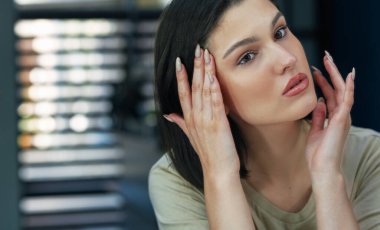 Yüzüne krem süren güzel bir dişinin yakın çekimi. Nemlendirici krem kullanan ve aynaya bakan esmer bir genç kadının samimi portresi..