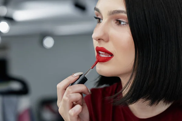 Closeup candid portrait of attractive young woman applying red lipstick. Brunette female with red lips making makeup and an online tutorial with beauty product.
