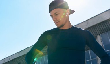 Spor kıyafetli bir sporcu, elleri belinde, güneş ışığında poz veriyor. Açık hava egzersizinden sonra ara veren bir sporcunun portresi.. 