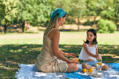 Mutlu, güzel bir kız ve annesinin battaniyede oturup parkta birlikte oynadığı uzun bir yatay manzara. Gülümseyen çocuk ve annesi yaz pikniği yapıyorlar. Anneler Günü..