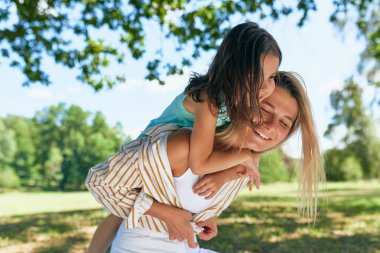 Mutlu anne ve kızı piknik sırasında parkta oynuyorlar. Mutlu kadın ve küçük kız, güneşli bir günde gülümsüyor ve birlikte vakit geçiriyorlar. Anneler Günü..