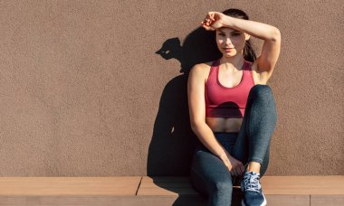 Güneşli bir günde açık havada antrenmandan sonra dinlenen genç bir kadının yatay görüntüsü. Athelete gülümseyen kız sabah güneşinin altında dinleniyor..