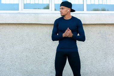 Sabahları sokakta dikilen bir sporcunun yatay görüntüsü. Yakışıklı sporcu sokakta mola veriyor, bir tarafa bakıyor..