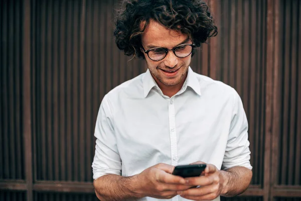 スマートフォン上で透明メガネメッセージングと白いシャツの成功した起業家の男の肖像画 男性は外のランチに同僚とオンライン会議を持っています — ストック写真