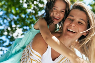 Piknik sırasında parkta oynayan neşeli bir anne ve mutlu kızının portresi. Mutlu kadın ve küçük kız, güneşli bir günde gülümsüyor ve birlikte vakit geçiriyorlar. Anneler Günü konsepti. 