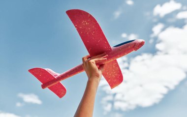 Gökyüzü arka planında bir kadının elindeki oyuncak bir uçağın yatay görüntüsü. Uçağı uçurmak için hazır tutan genç bir kadın. Seyahat kavramı.
