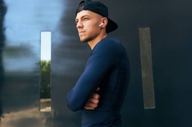 Atletik bir adamın şehir sokaklarında antrenman yaptıktan sonra ara verdiği son manzara. Spor giyimli ve şapkalı bir erkek sporcu kollarını kavuşturuyor..