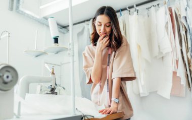 Bir terzi, çevrimiçi bir mağaza için yeni bir elbise ilanı veriyor. Yaratıcı ofisinde yeni bir koleksiyon için çalışan genç bir kadın işyeri sahibi..