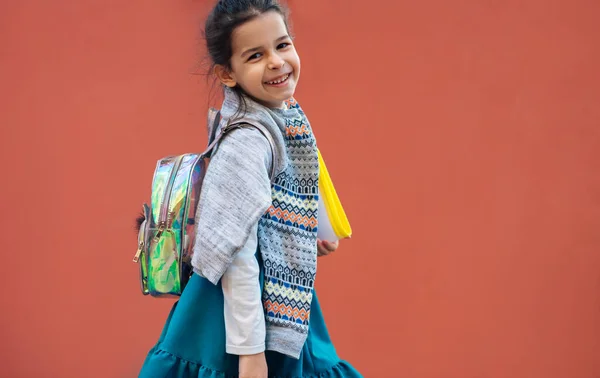 学校に行く笑顔の子供の水平画像 オレンジの背景にポーズ かなり小さな女の子ですバックパックとフォルダ屋外で歩く — ストック写真