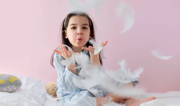 Niña Bonita Pijama Soplando Plumas Blancas Mientras Juega Cama Sobre — Foto de Stock