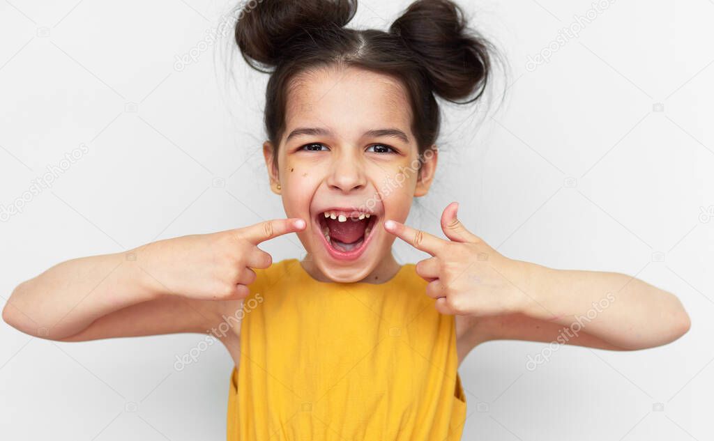 Happy preschooler little girl in yellow dress showing empty space with growing first permanent molar isolated on grey studio background. Cute kid missing primary baby tooth. Child has lost milk tooth.