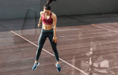 Güneşli bir günde, spor yaparken atlayan bir kadının yatay görüntüsü. Dışarıdaki spor kıyafetlerinde formda bir kadın..