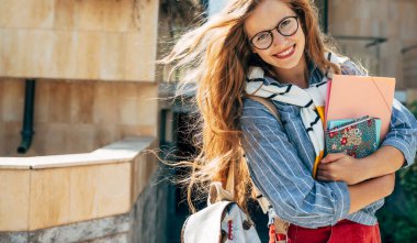 Uzun kızıl saçlı, gülümseyen, şeffaf gözlükler takan ve güneşli bir günde yanında bir sürü kitap ve klasör taşıyan mutlu bir genç kızın portresi..