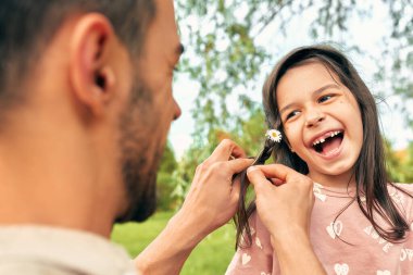 Sevgi dolu bir babanın güzel kızına papatya çiçekleri ören bir saç modeli. Mutlu bir çocuk babasıyla parkta vakit geçirir..
