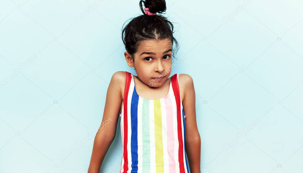 Little girl wearing colorful swimwear, poses over blue studio background.
