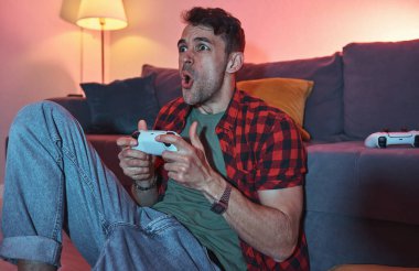 Evinde oyun alanı olan oyuncu bir adam online video oyunu oynuyor. Oyuncu erkek, oturma odasında yerde oturmuş oyun oynuyor..