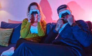 Evde video oyunu oynayan ve eğlenen çift yüzlerini joystickle kapatıyor. Olumlu arkadaşlar evde video oyunu oynarken eğleniyorlar. Video oyunu oynayan iki genç.