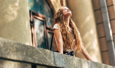 Uzun saçlı, yukarı bakan güzel bir kadının açık hava görüntüsü. Şehirde poz veren genç bir kız öğrenci..