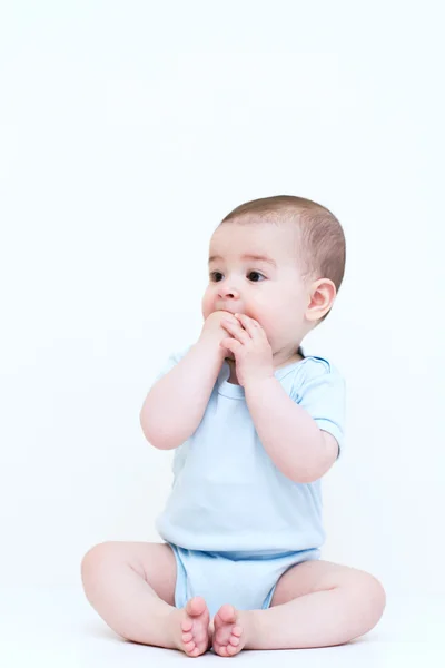 Сидя на белом фоне, красивый ребенок с руками во рту — стоковое фото