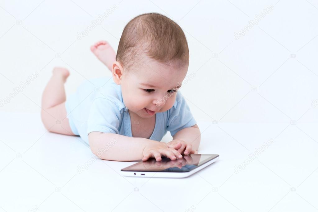 Happy baby plying with a tablet on white floor