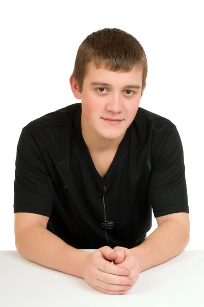 De jonge man zit aan een tafel in een zwart shirt op een witte achtergrond — Stockfoto