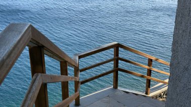 Sakin mavi okyanusa giden tahta merdiven kayalık kıyı şeridi boyunca iniyor.