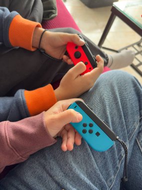 Renkli kumandaları tutan eller, ortak oyun eğlencesini öneriyor. Rahat koltuklar rahat ve keyifli atmosferi ima eder. Arkadaşlar oyun oynayarak bağ kurar, kahkaha ve heyecan paylaşır