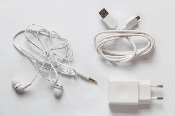 Beyaz akıllı telefon şarj cihazı, Usb kablosu ve beyaz zemin üzerine beyaz kulaklık.