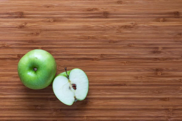 Manzana verde madura fresca Granny Smith: entera y cortada por la mitad en una tabla de cortar de madera. Concepto de fruta natural. Antecedentes para temas de dieta saludable . — Foto de Stock