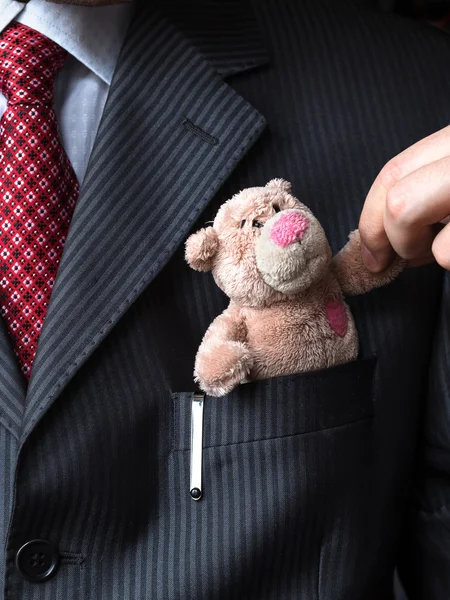 L'élégant homme d'affaires élégant gardant ours en peluche mignon dans une poche de son costume de poitrine. Une main qui serre la patte d'un ours en peluche. Concept formel de négociation . — Photo