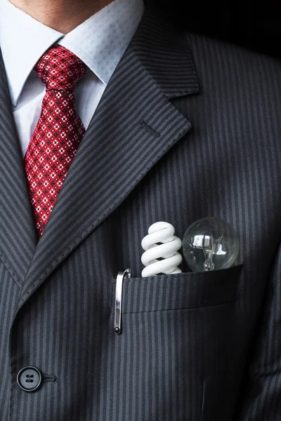 El elegante hombre de negocios elegante que mantiene dos bombillas diferentes - eficiencia energética incandescente y fluorescente - en el bolsillo de su traje de pecho. Concepto de ahorro energético. Tema de protección del medio ambiente . — Foto de Stock